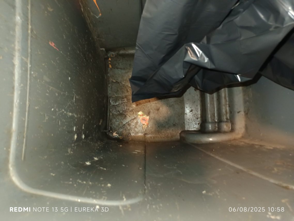 Conteneur sale avec des déchets au fond et des objets obscurcis par l'ombre.